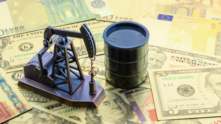 Oil pump jack and barrel placed on top of international currency notes symbolizing global oil trade and economic impact.